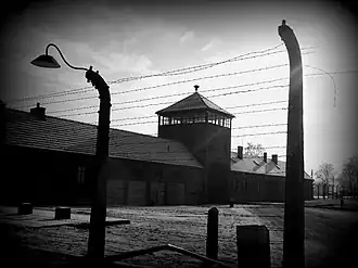 Photo en noir et blanc montrant derrière des barbelés un long bâtiment avec un mirador au milieu