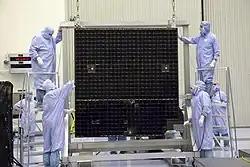 Un panneau solaire suspendu à un cadre et entouré de techniciens