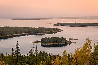 Vue d'un golfe parsemé d'île lors d'une nuit polaire, entourée de forêts aux tons automnals.