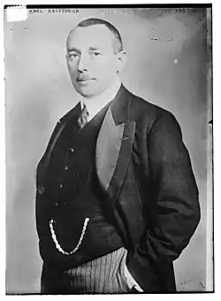 Photo en noir et blanc de profil d'un homme en costume, il porte une petite moustache et des cheveux courts
