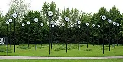 Dans un parc se trouvent des horloges à la même heure surmontant chacune un poteau. Les poteaux sont en rang. C'est Zeitfeld, une installation de 1987 au Südpark de Düsseldorf.