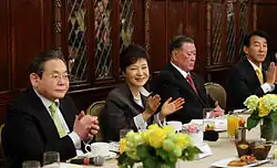 Photographie d'un banquet, au centre Park Geun-hye est en train d'applaudir entourée par trois hommes âgés.