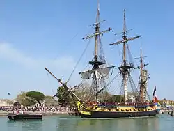 Photographie d'un navire à trois mâts escorté par une vedette.