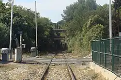 Une entrée de tunnel au loin, la voie ferroviaire qui y mène traverse d'abord un passage à niveau.