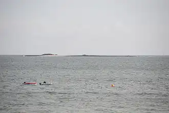 Vue en couleur d'une île plate en arrière plan d'une étendue d'eau, montrant deux barques.