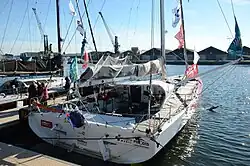 Au ponton, voilier blanc à l'arrière, rouge à l'avant, vu de trois quarts arrière.