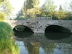 Pont à deux arches en pierre et béton au-dessus du contre fossé.