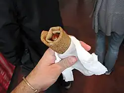 Photographie montrant une main humaine, tenant une saucisse enroulée dans une galette.
