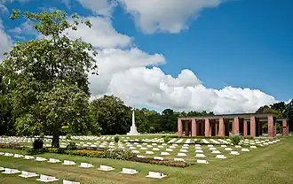 Photo couleur. Cimetière avec des rangées de pierres tombales. Croix et structure en briques rouges en arrière-plan.