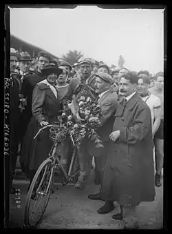 Photographie en noir et blanc d'un coureur recevant un bouquet de fleurs et entouré par la foule.