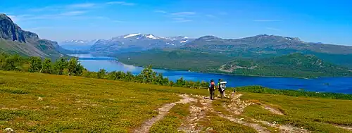 Deux randonneurs marchant vers un cours d'eau, au milieu d'un paysage montagneux.