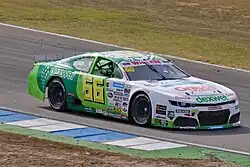 Photographie d'une voiture de NASCAR blanche sur l'avant, vert pomme à l'arrière, vue de trois-quarts droit, sur une piste sèche.