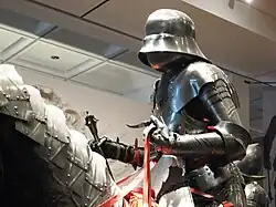 Un mannequin portant une armure de plates et tenant une masse d'armes.