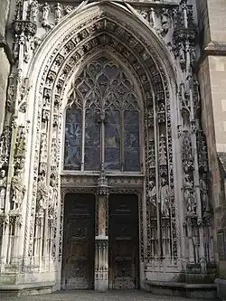  Grand Portail, ou portail de Montfalcon, entièrement restauré en 1892-1909. Porte principale à double battant avec trumeau à niche vide, créé à cette époque.