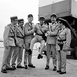 Six comédiens en tenue de gendarmes, debouts, côte à côté, hilares, Louis de Funès est porté par les deux plus grands, Marin et Grosso.