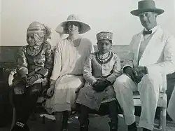 le roi et la reine en vêtements clairs posent assis sur un banc en compagnie de deux enfants