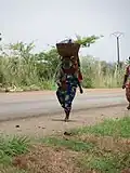 Femme marchant pieds nus, avec bébé au dos se rendant au marché sous un soleil ardent à Pobè au Bénin.