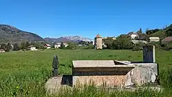 Vue de la vallée de Lus dans les environs du village. Au premier plan, une fontaine au bord d'un pré ; au second plan, le hameau des Corréardes ; à l'arrière-plan, le Jocou (2051m).
