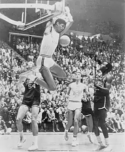 Lew Alcindor, suspendu au panier, sous les yeux d'adversaires et de coéquipiers.