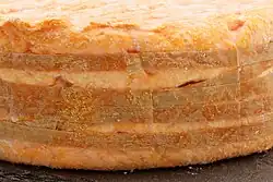 Photo couleur en gros plan d'un détail de fromage de couleur orange et petits points blancs à aspect visqueux entouré de bandelettes.