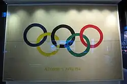 Photographie montrant un drapeau blanc sur lequel figurent les anneaux olympiques et le texte « ALEXANDRIE 5 AVRIL 1914 ».