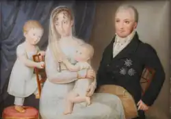 Huile sur toile représentant Louis-Philippe, tête-nue, en habit noir sur un pantalon crème, Marie-Amélie en robe perle les cheveux recouverts d'un léger voile long, tenant Louise sur ses genoux et Ferdinand derrière elle.