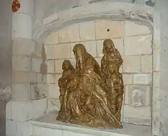 Vue de côté d'un groupe sculpté en bois placé dans une niche d'un mur en pierre.