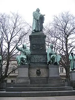 Statue monumentale avec un personnage début à son sommet et deux personnages assis à la base, un côté droit, l'autre côté gauche