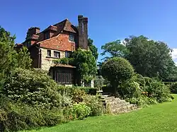 Photo en couleurs d'une maison en pierres blanches et en briques rouges entourée d'un jardin verdoyant