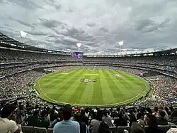 Vue panoramique de l'intérieur d'une enceinte sportive avec des tribunes remplies avant une rencontre de cricket.