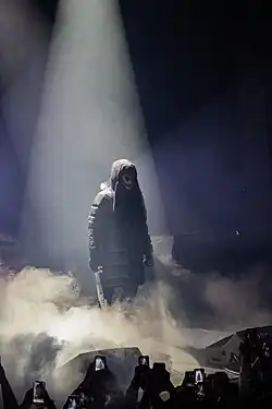 L’artiste menace Santana au centre, entouré de fumée, tenant une machette dans sa main droite gravée à son nom, tenant un micro dans sa main gauche