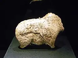 Photographie en couleurs sur fond noir d'une statuette en ivoire posée sur un socle anthracite et représentant le corps d'un bison.
