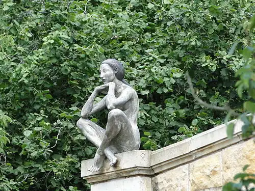 Sculpture en bronze représentant une femme assise en tailleurs sur la rampe d'un escalier monumental.