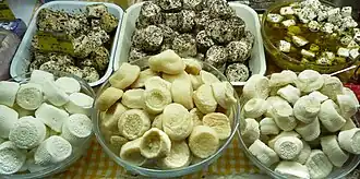 la photographie couleur montre un assortiment de fromages dans des bols en verre posés sur une nappe vichy jaune. Au premier plan, trois bols contiennent des fromages nature frais, demi-secs et secs, alors qu'à l'arrière plan, trois bols contiennent des fromages aromatisés aux herbes ou macérés dans l'huile d'olive.