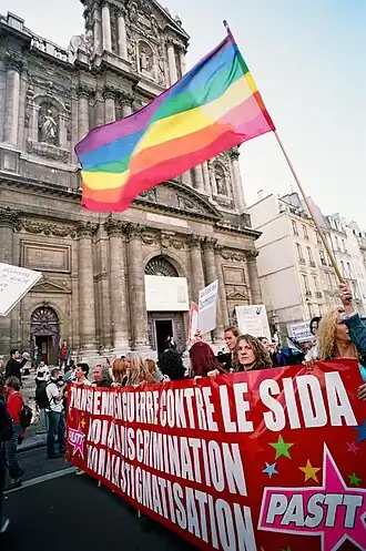 Front d'une marche avec un drapeau LGBT et une banderole sensibilisant contre les discriminations.