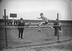 Photographie en noir et blanc d'une athlète féminine sautant au-dessus d'une barre.