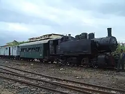 Locomotive à vapeur noire dans la gare de Massaoua tirant deux wagon vert et blanc.