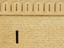 Photographie montrant une ligne de merlons arrondis, au-dessus d'une ouverture en forme de meurtrière.