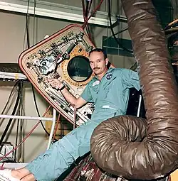 Photographie couleur de Collins assis sur l'écoutille de son module et tenant le panneau ouvert.