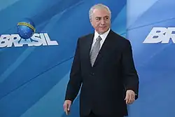 Michel Temer sorrindo. O fundo é azul e contém o símbolo de seu governo.