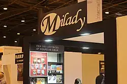 Photographie en couleurs d'une partie de hall d'exposition, montrant principalement une enseigne et plusieurs livres exposés