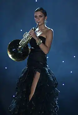 Une fille debout en robe sans bretelles joue du cor d'harmonie.