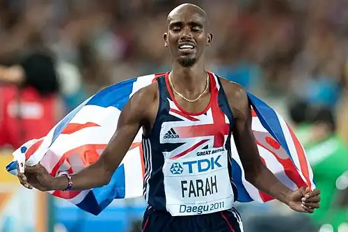 Mo Farah tenant un drapeau britannique qui flotte dans son dos.