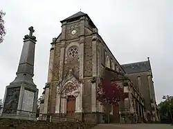 Photographie en couleurs de la façade d'une église avec un monument aux morts au premier plan.