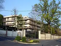 Immeuble moderne de trois étages, au murs blancs, avec terrasse, et entouré d'arbres.