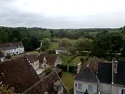 Photographie en couleurs d'un cours d'eau bordé de prés et d'arbres en arrière-plan de maisons aux toits de tuile.