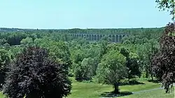 Photographie en couleurs d'un viaduc traversant en arrière-plan une vallée boisée.