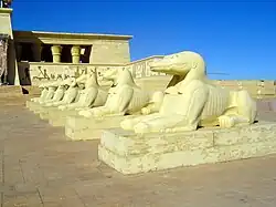Décor de cinéma défraîchi, représentant un palais égyptien et une rangée de sphinx à têtes de crocodiles.