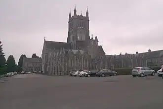 Photographie en noir et blanc d'une église néogothique en pierres dotée d'une tour-clocher massive.