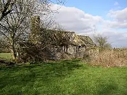 Photo d'un petit bâtiment en mauvais état, au toit percé et aux fenêtres béantes, à moitié dissimulé par un arbre